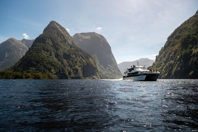 A day cruise boat under way on dark water below steep forested peaks