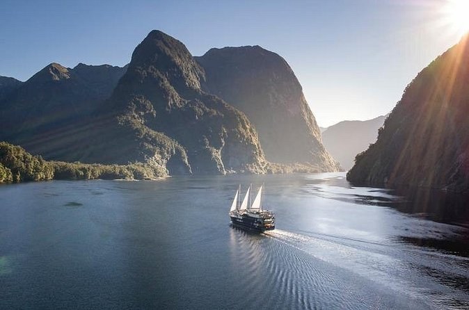 A sailing ship crossing a fiord between steep peaks, seen from above