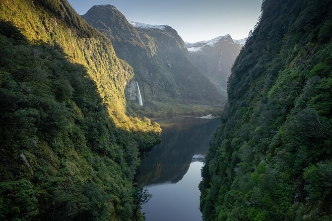 A narrow fiord arm between sheer green walls, a waterfall on the far side