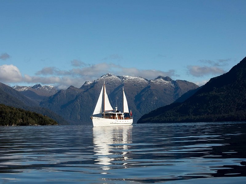 A two-masted yacht on a calm lake below snow-dusted ranges